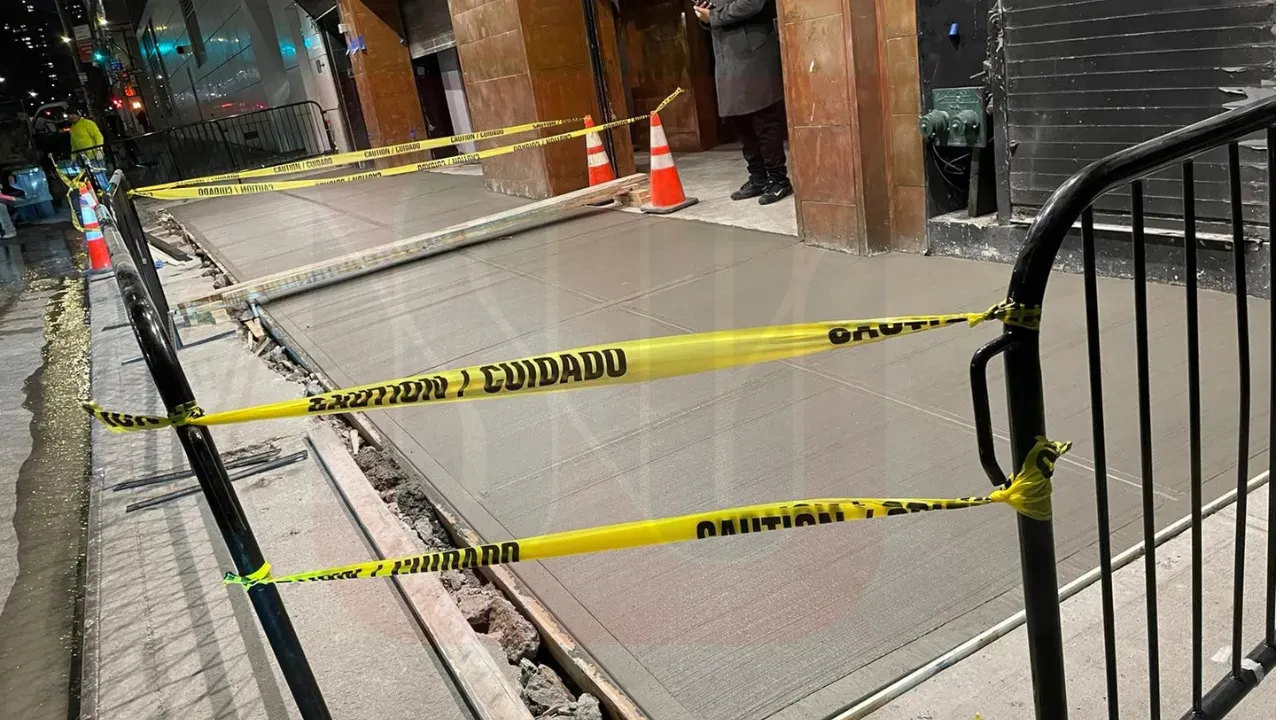 Fresh concrete being poured onto a sidewalk, with workers spreading and leveling the mixture
