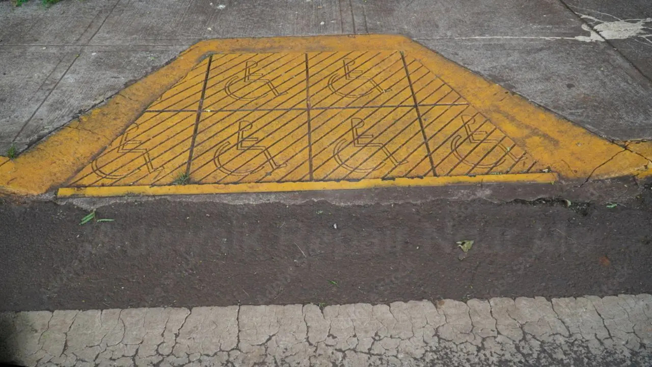 Is a Permit Required for Curb Cut Repairs in NYC? Yellow-painted curb cut with accessible wheelchair markings on a sidewalk, showing a designated ramp for accessibility compliance.