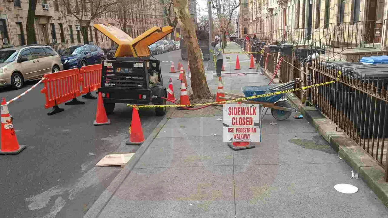 Freshly poured concrete on a sidewalk section marked by traffic cones and caution tape, with a sign indicating the sidewalk is closed and directing pedestrians to use an alternate walkway